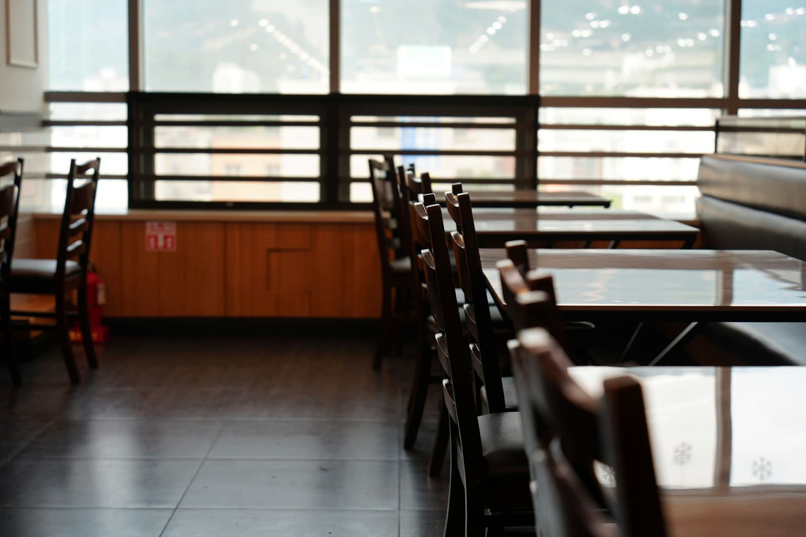 Comedor de restaurante vacío con mesas y sillas de madera preparadas junto a un gran ventanal
