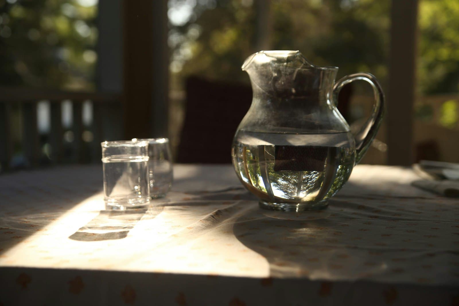 Jarra de cristal con agua y dos vasos sobre una mesa con luz de tarde