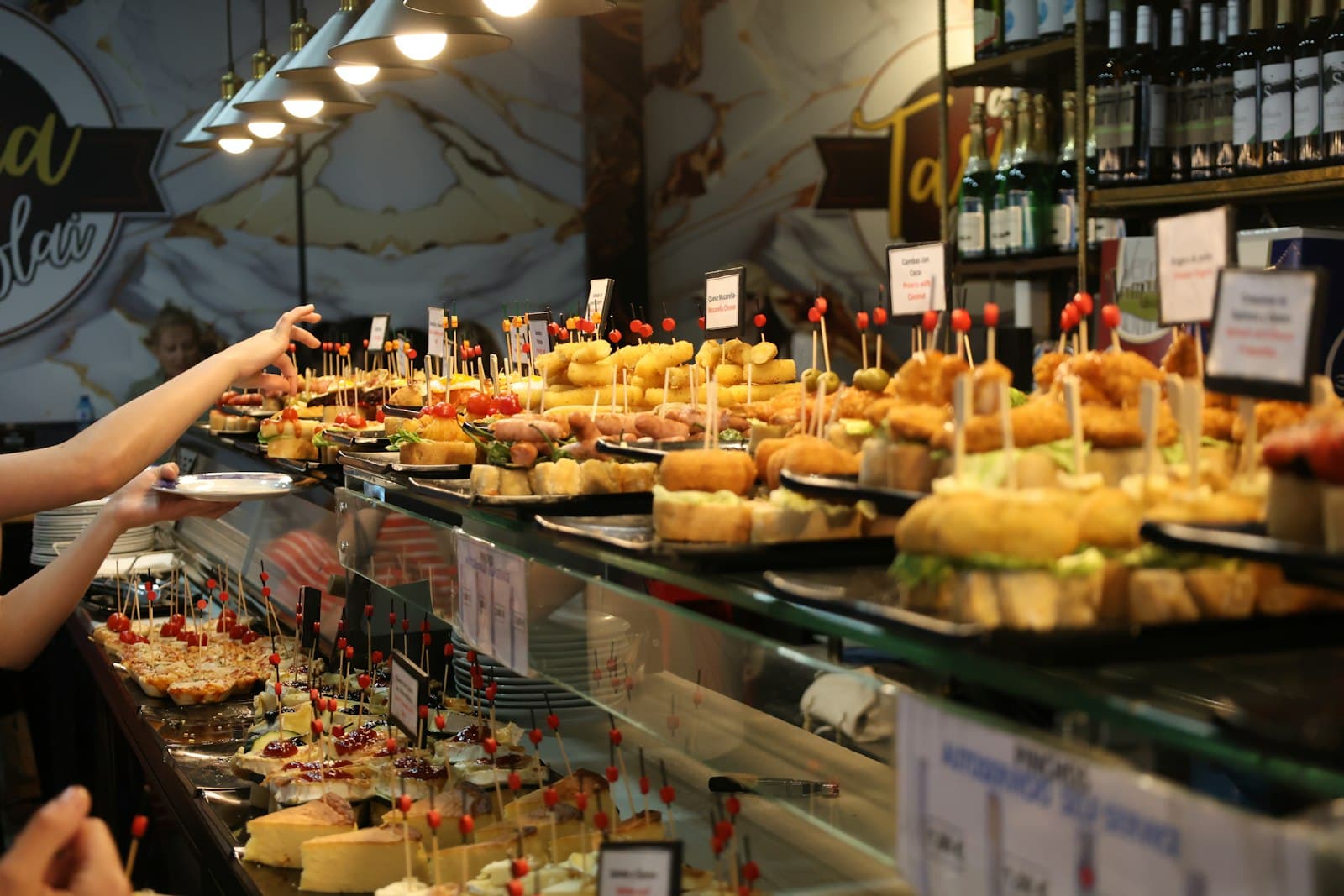 Barra de un bar de pintxos en Barcelona llena de tapas mientras los clientes se sirven