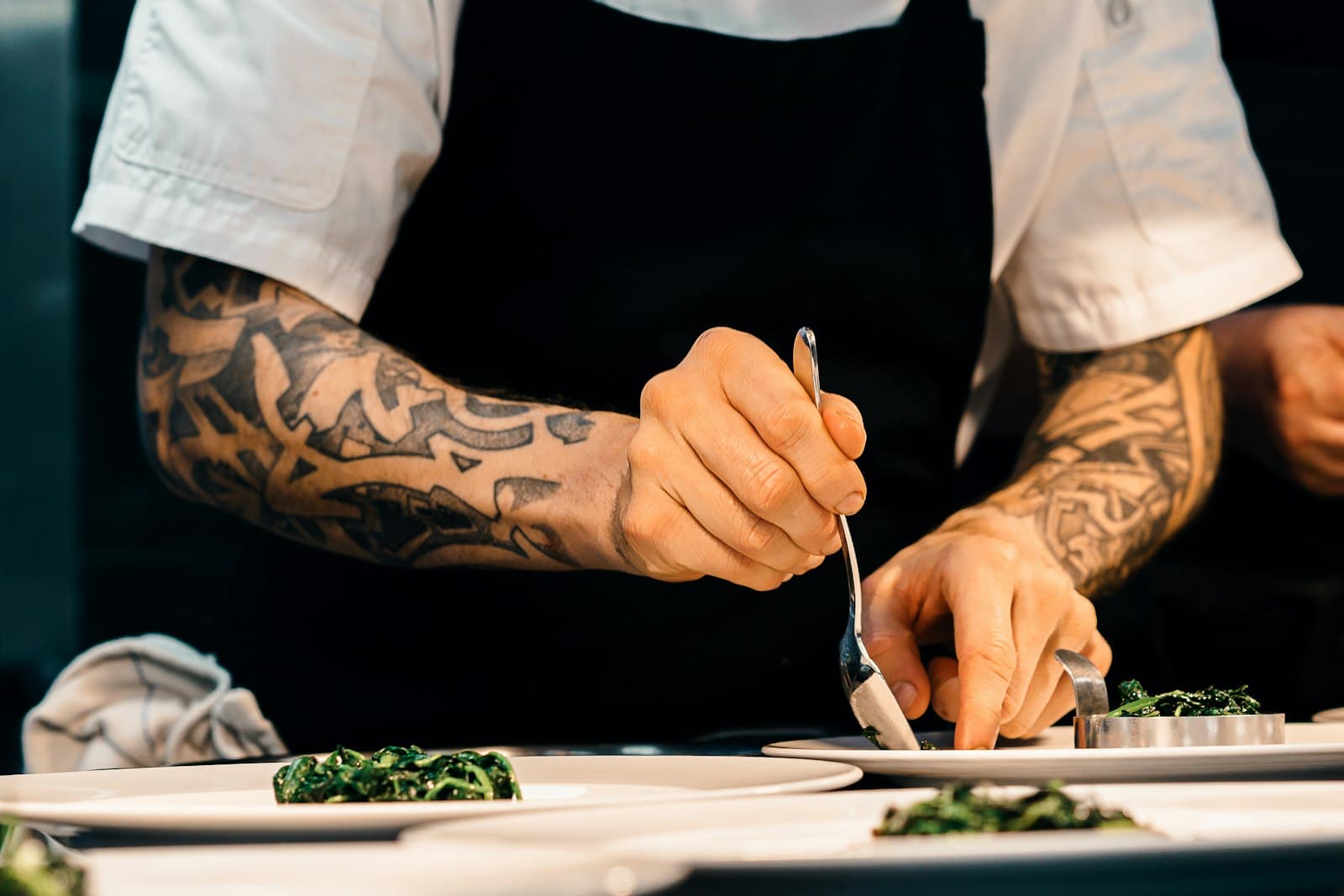 Cocinero con delantal negro emplatando verduras con una cuchara en la cocina de un restaurante
