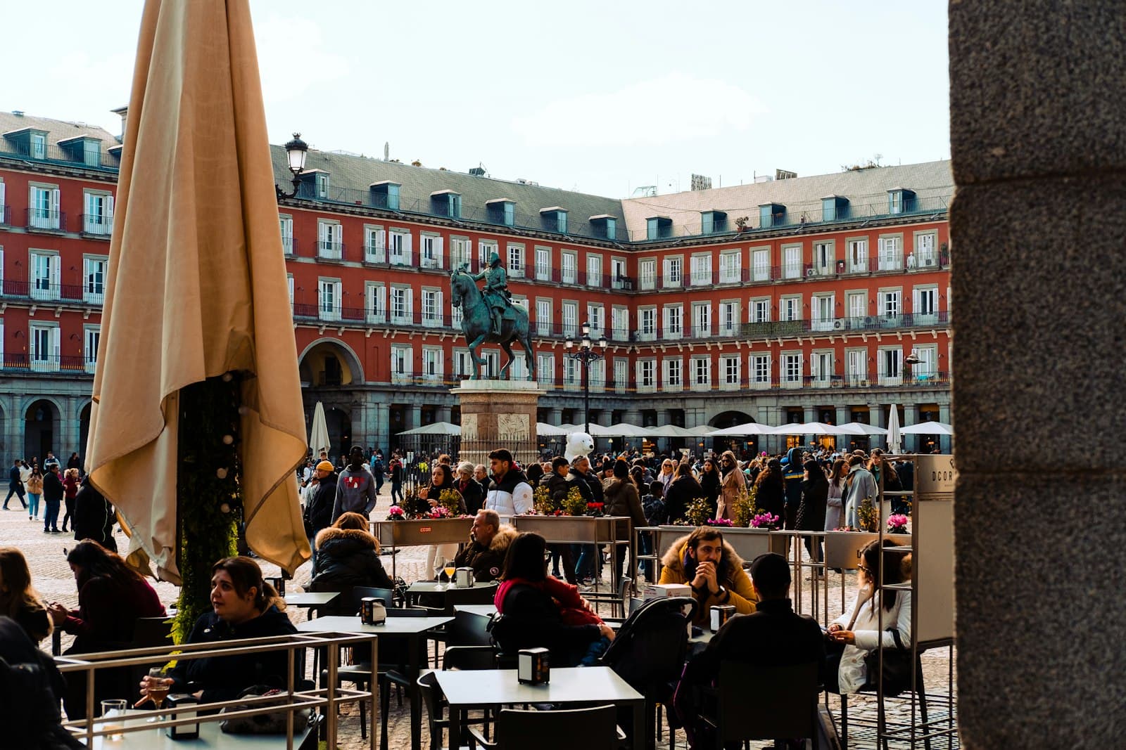 Terrazas llenas de gente en la Plaza Mayor de Madrid con soportales y la estatua ecuestre al fondo