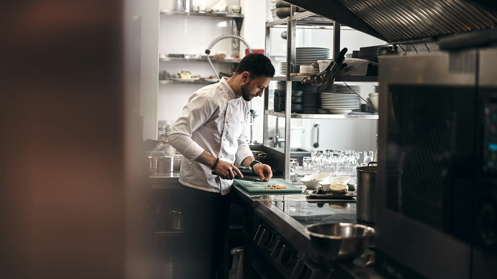 Cocinero con chaquetilla blanca cortando verduras en una tabla en la cocina de un restaurante
