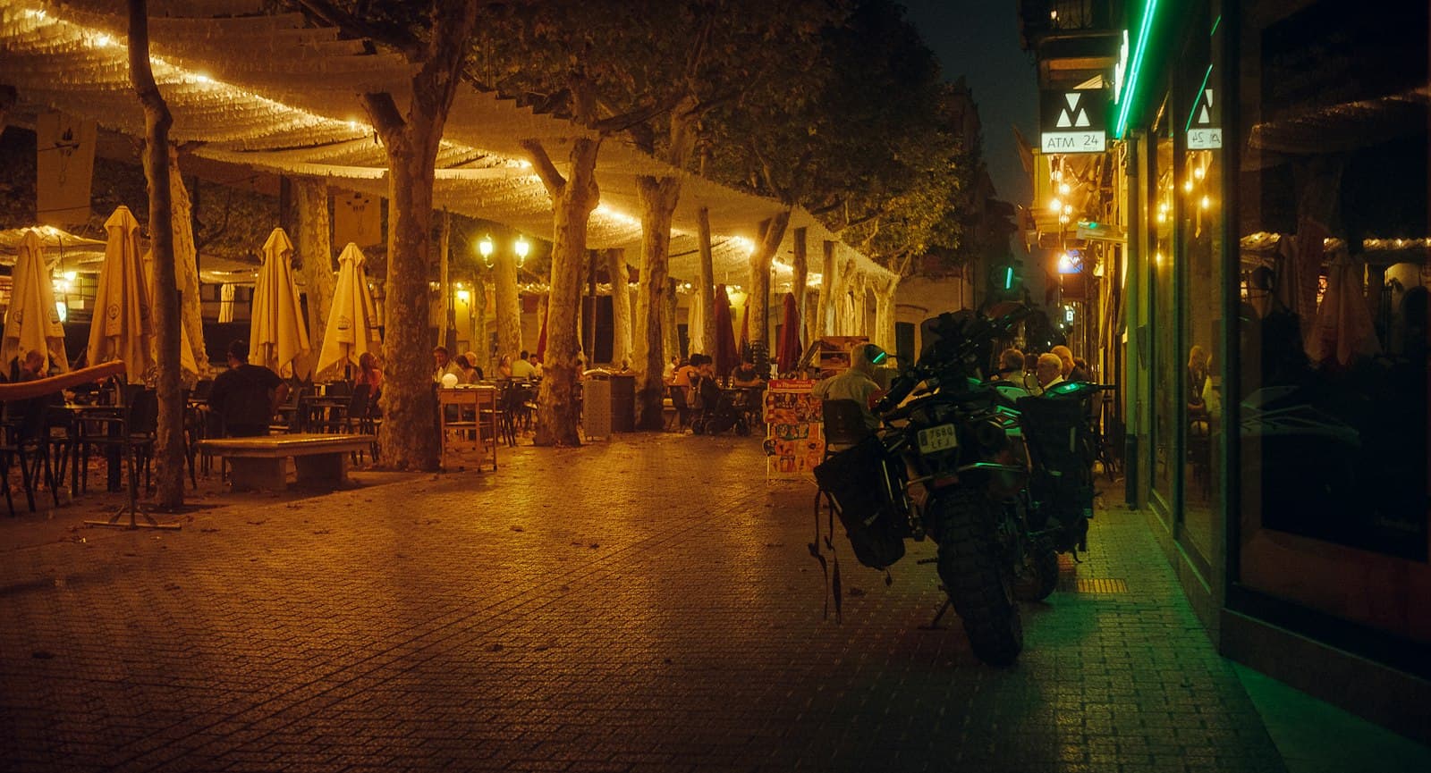 Calle peatonal de Mallorca de noche, con terrazas bajo toldos iluminados y una moto aparcada junto a los locales
