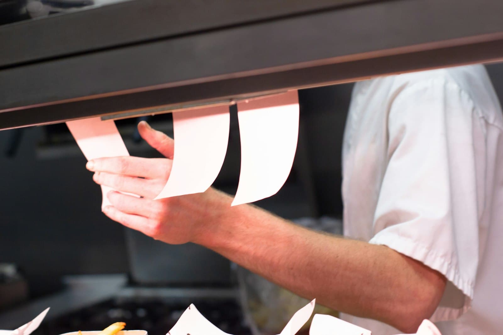 Cocinero cogiendo comandas en papel colgadas del raíl del pase en una cocina