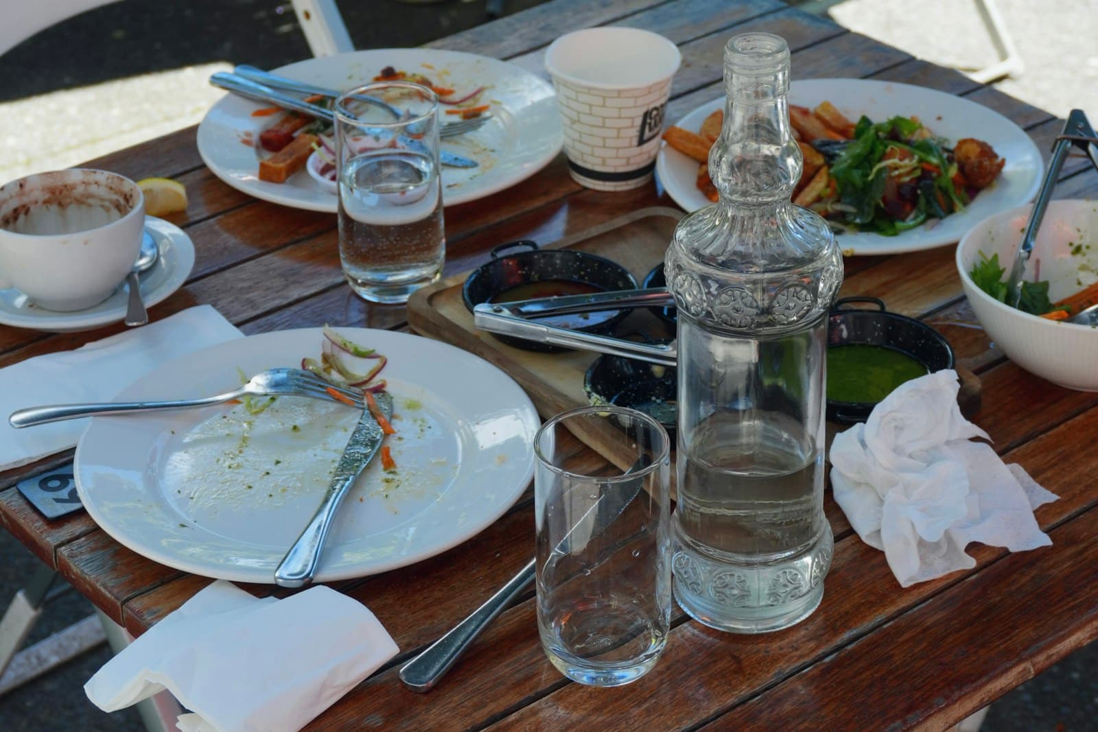 Mesa de terraza con platos a medio terminar, vasos y una botella de agua después de comer