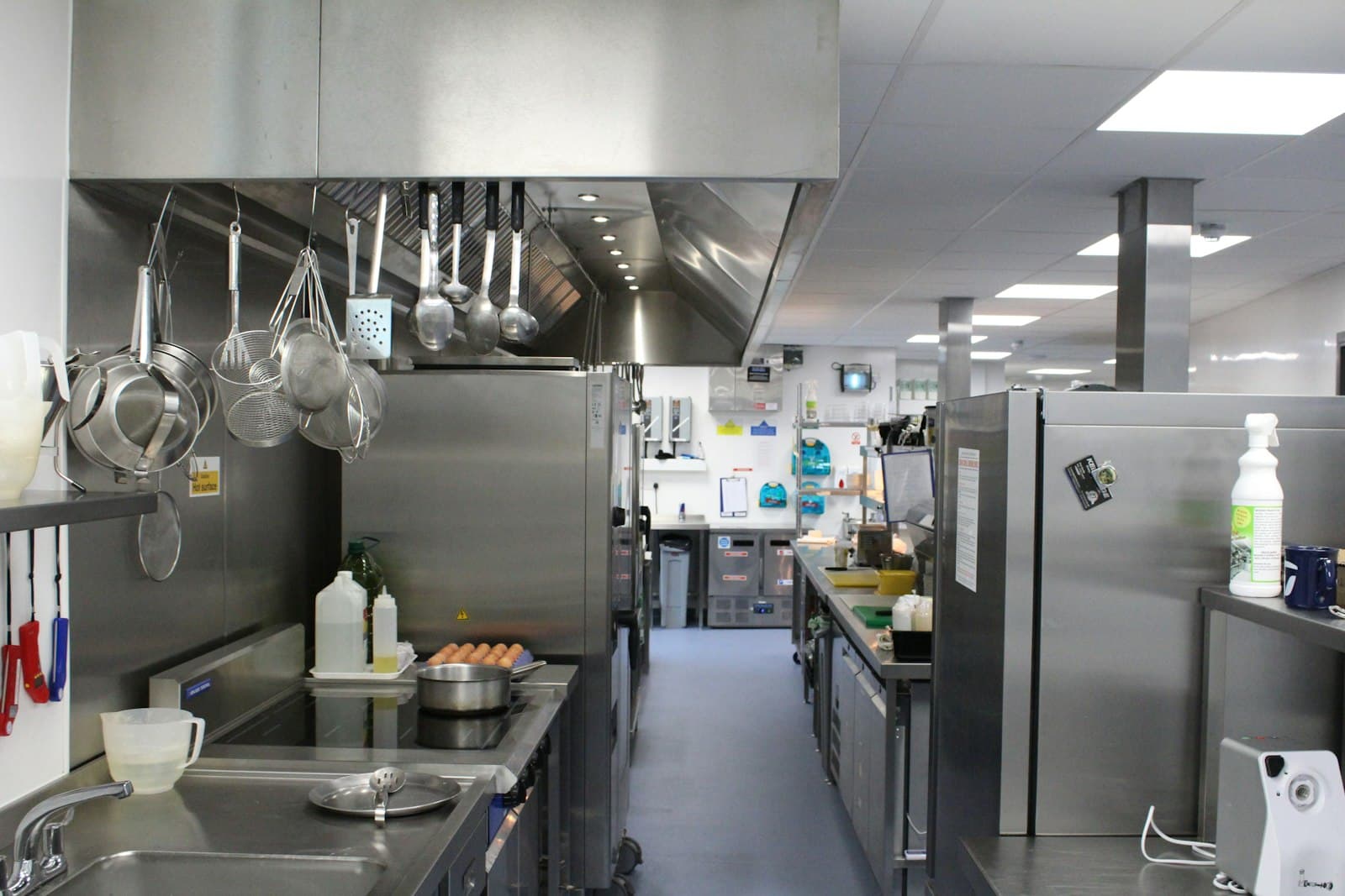 Cocina profesional de acero inoxidable con cámaras frigoríficas, utensilios colgados y un pasillo central