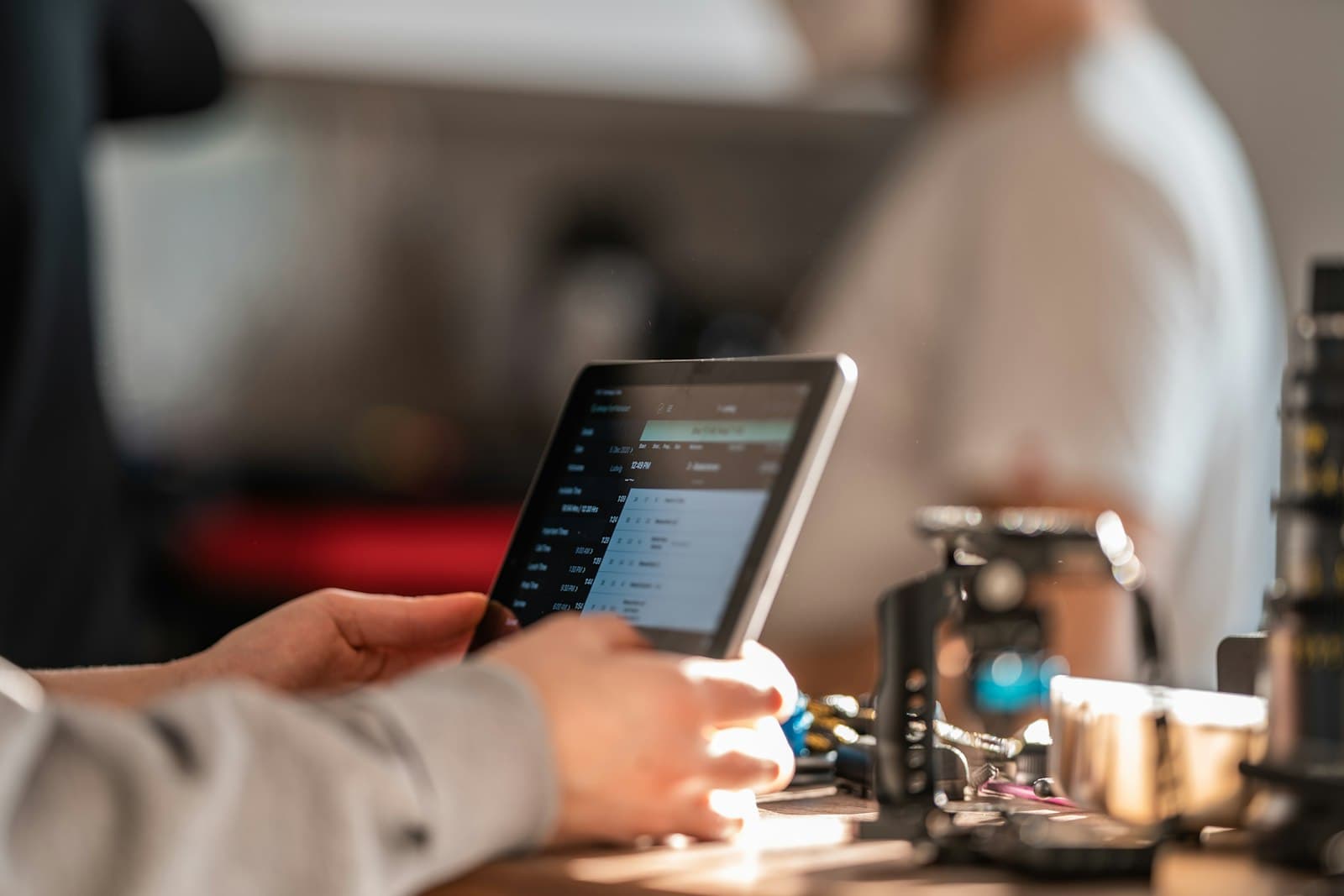 Manos de un camarero usando una tablet de TPV junto a la cafetera en la barra