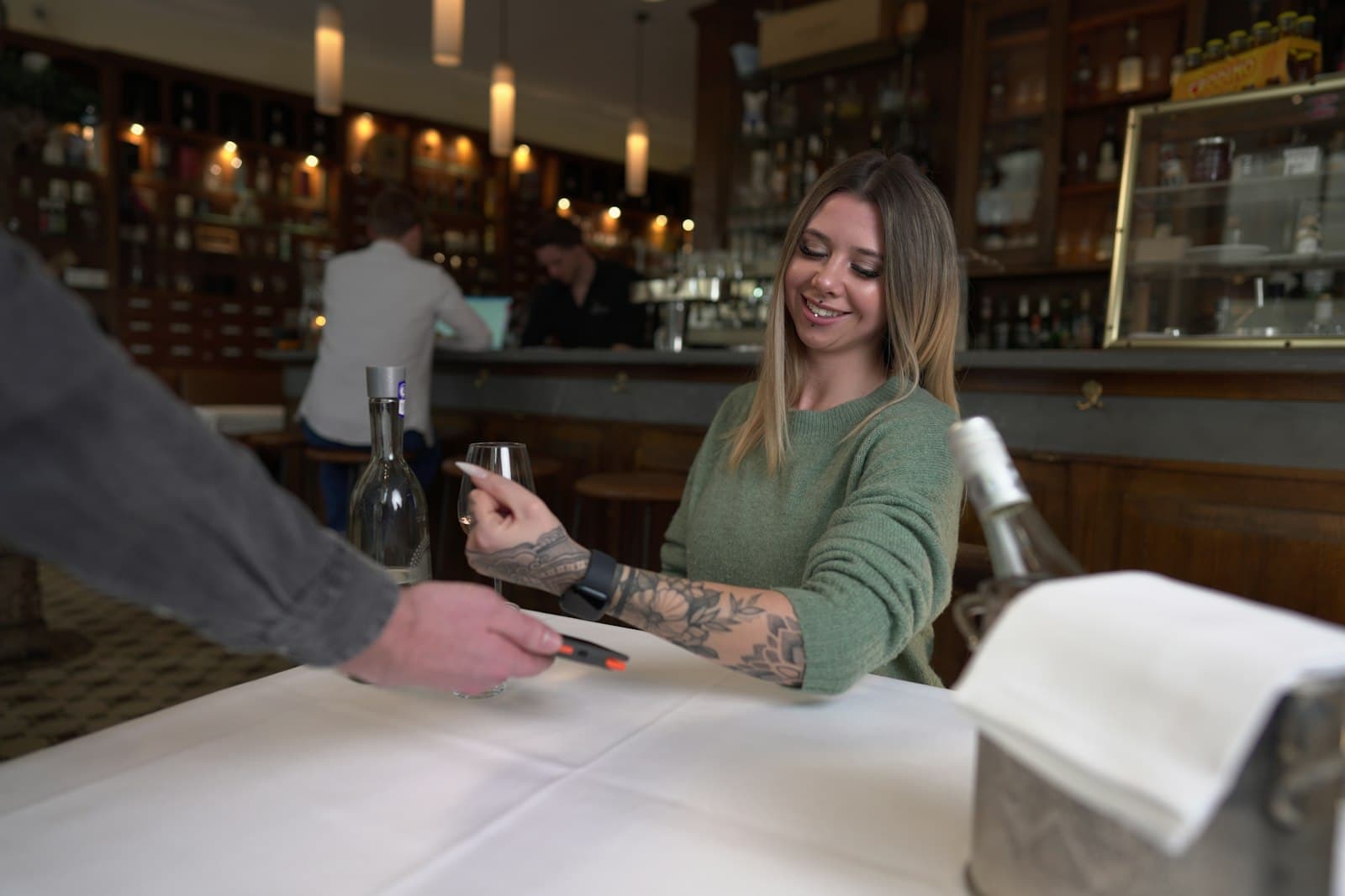 Camarero acercando el datáfono a una clienta sonriente que paga en la mesa de un restaurante