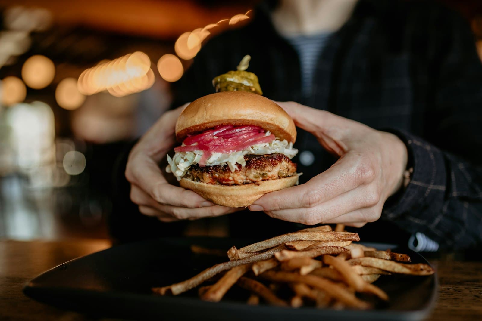 Persona sujetando con las dos manos una hamburguesa con patatas fritas en un restaurante