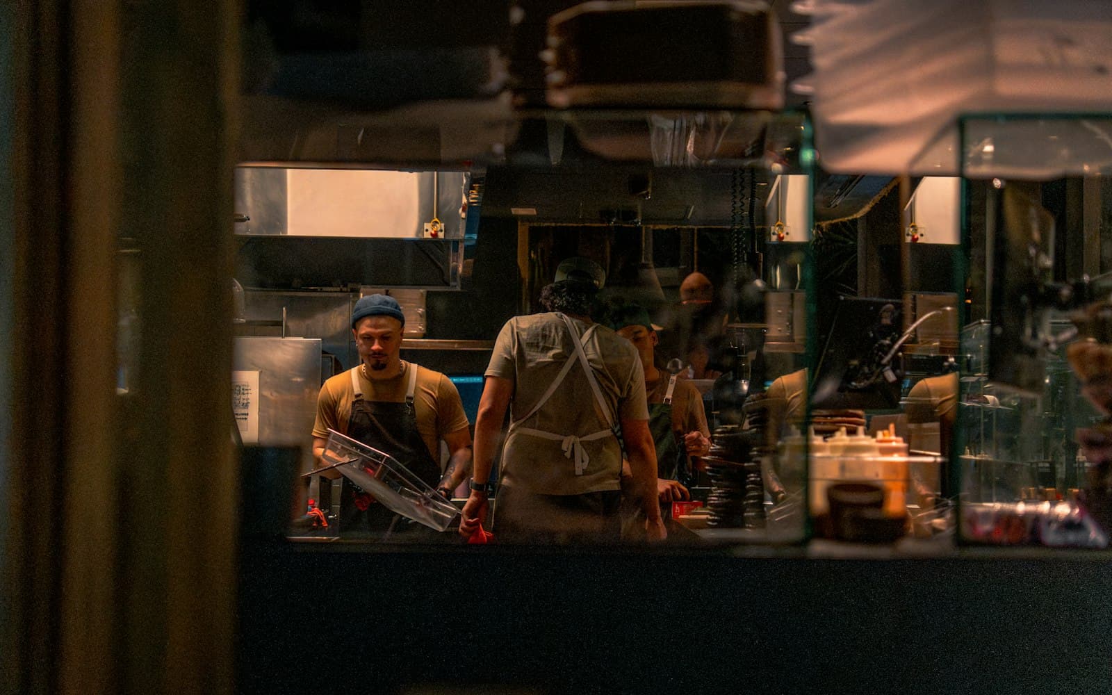 Equipo de cocina trabajando de noche detrás del pase de un restaurante, visto desde fuera