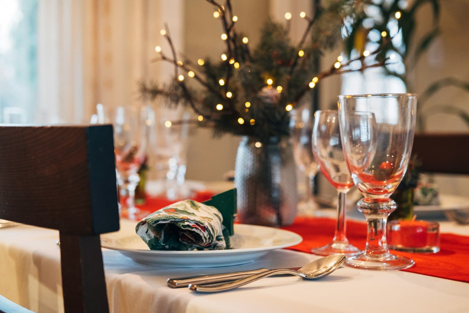 Mesa puesta para una cena de Navidad con copas, servilleta estampada y ramas con luces de colores