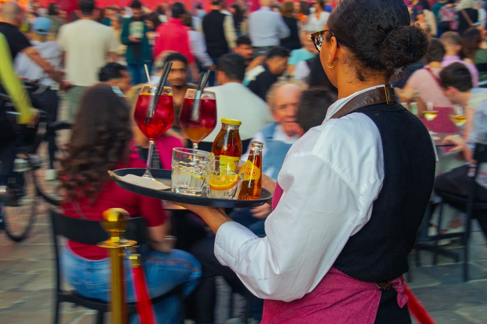 Camarera llevando una bandeja con bebidas entre las mesas de una terraza llena
