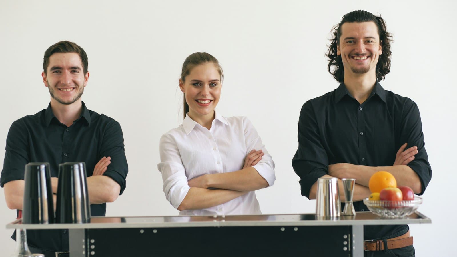 Tres camareros sonrientes con uniforme detrás de la barra de un bar