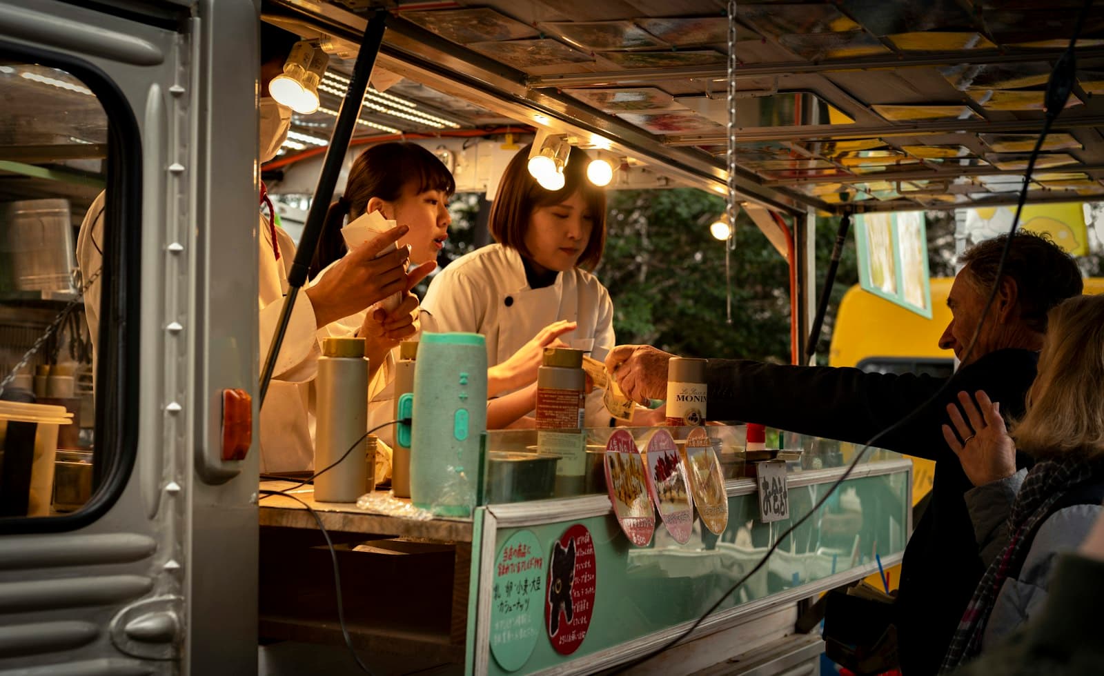 Dos cocineras atienden a los clientes desde la ventanilla iluminada de un food truck por la noche