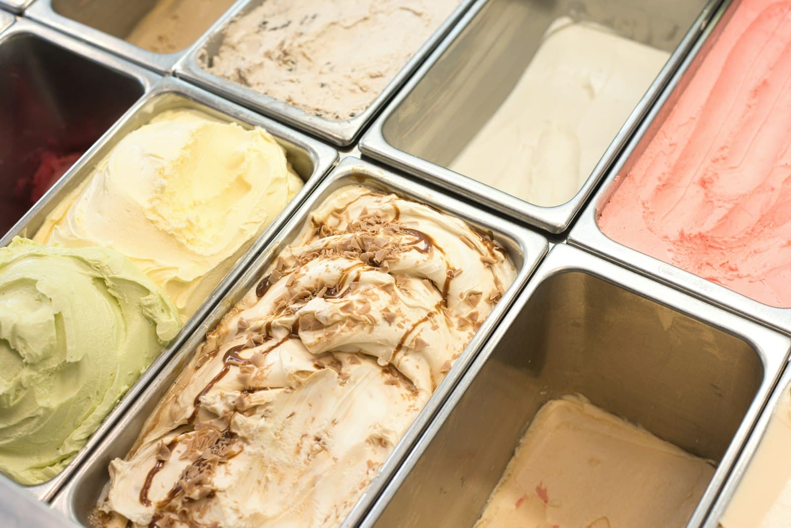 Cubetas de acero con helados de varios sabores en la vitrina de una heladería, algunas casi vacías