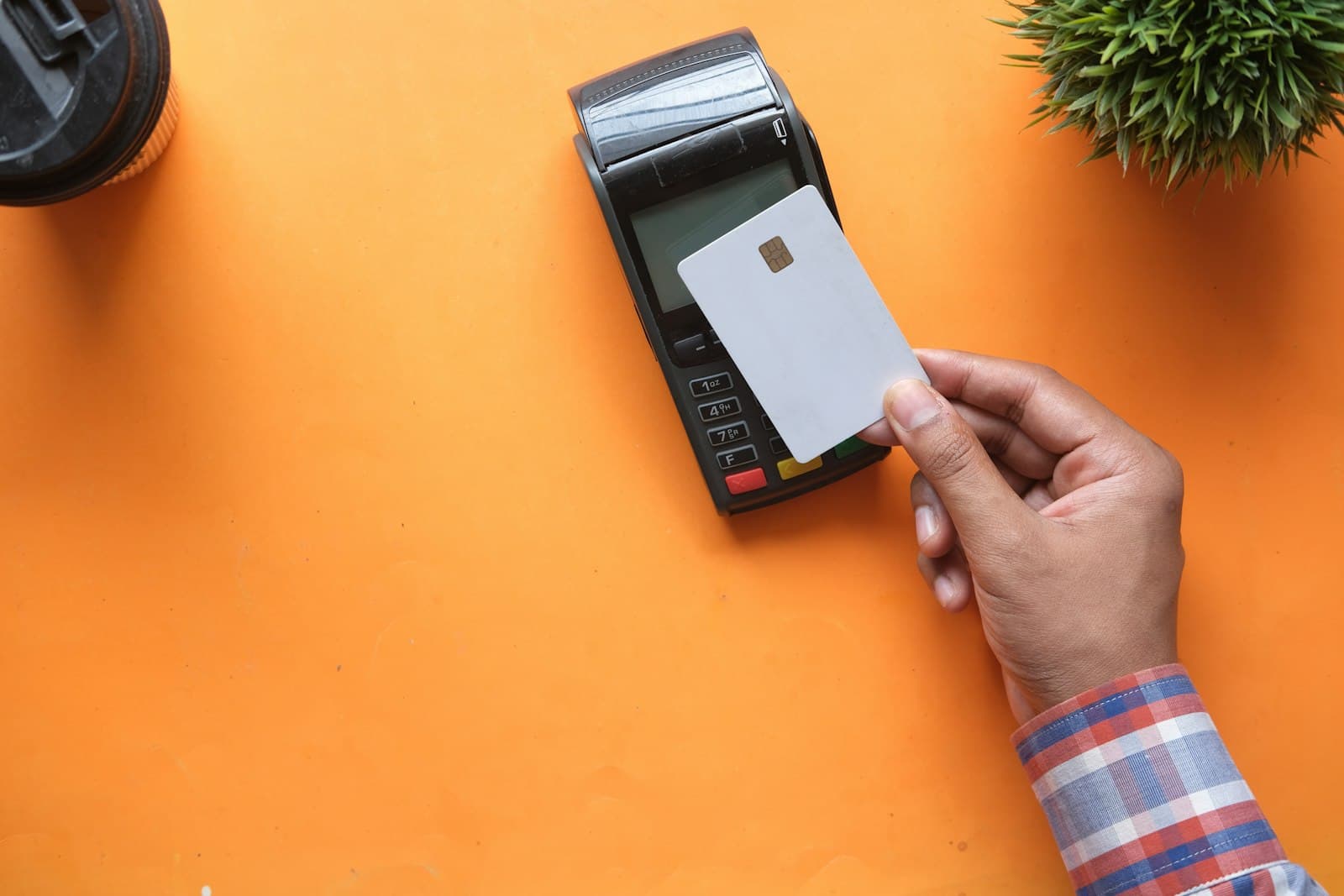 Mano acercando una tarjeta a un datáfono sobre una mesa naranja