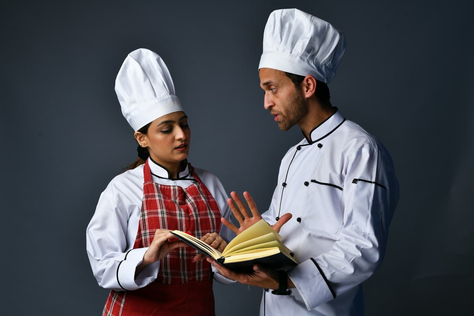 Una cocinera y un cocinero repasan juntos las notas de un cuaderno