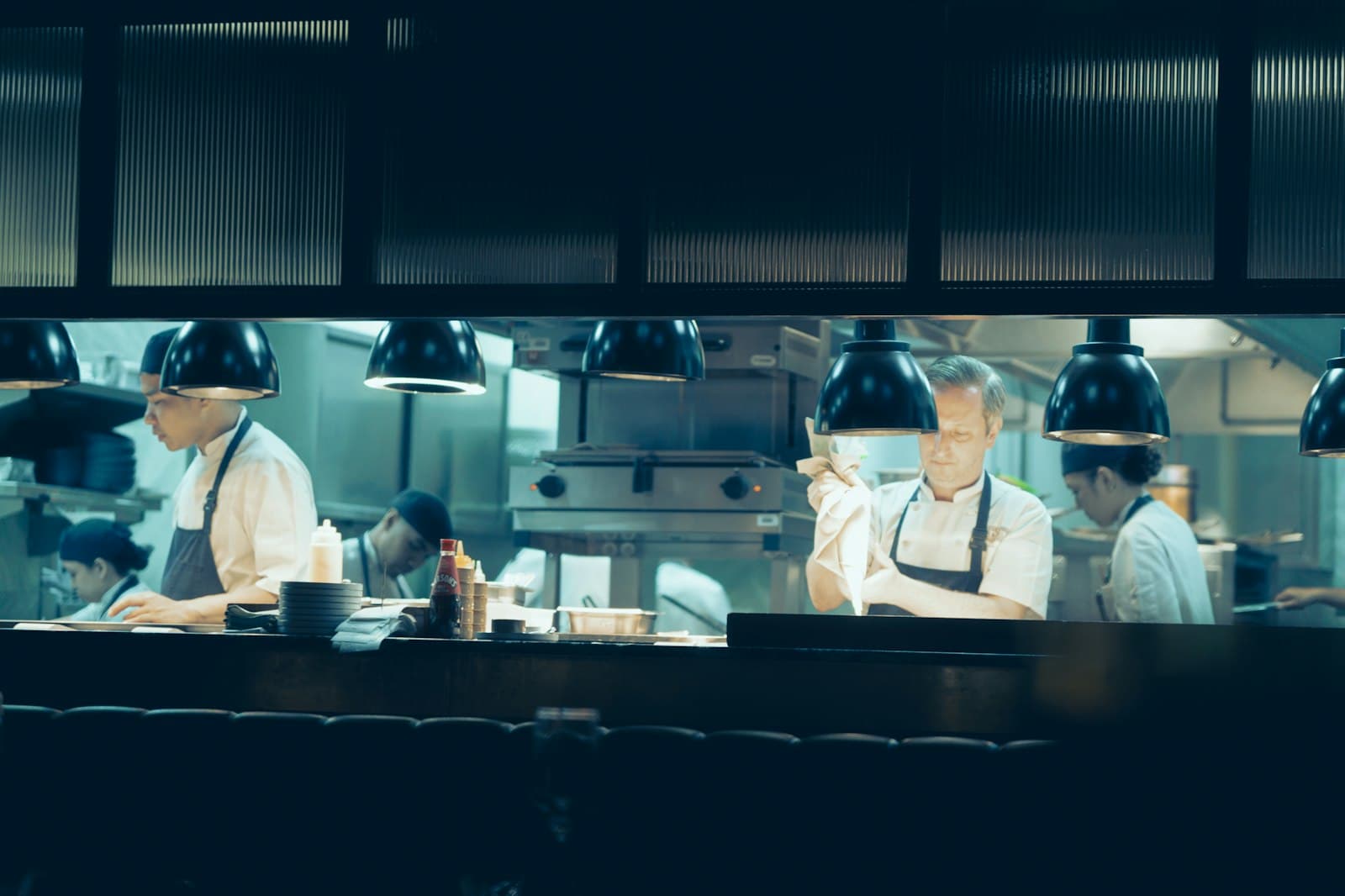 Equipo de cocineros trabajando bajo las lámparas del pase en una cocina profesional