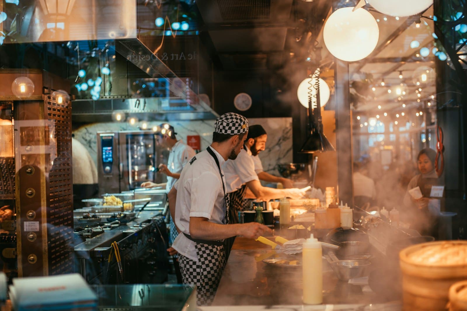 Cocineros trabajando en una cocina abierta con vapor durante el servicio de noche