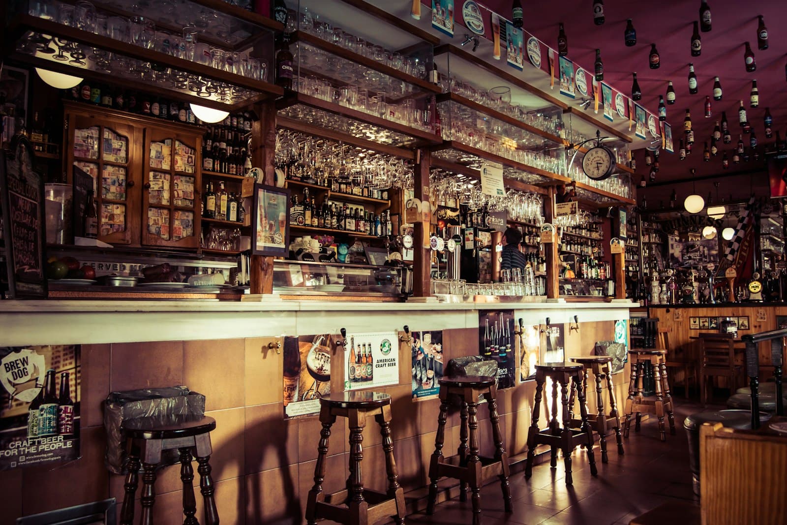 Barra de un bar clásico con taburetes de madera, botellas en las estanterías y vasos colgados