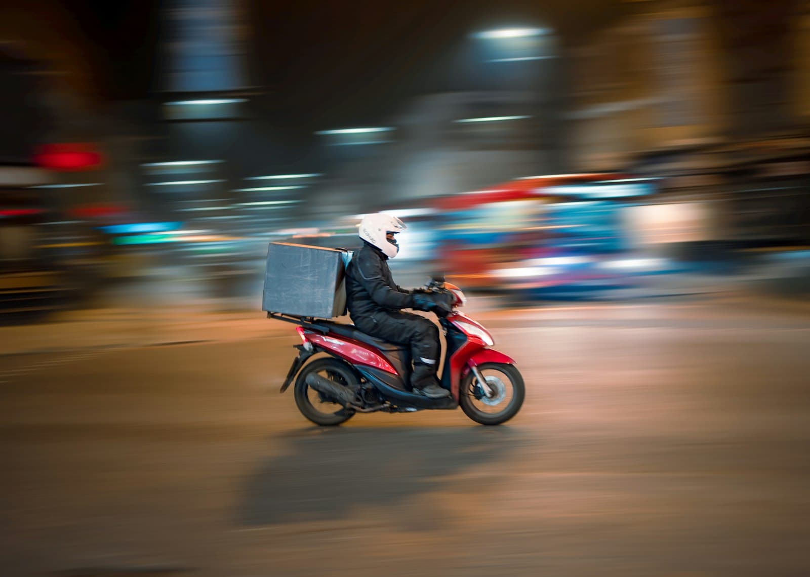 Repartidor en moto roja con caja de reparto circulando de noche por la ciudad