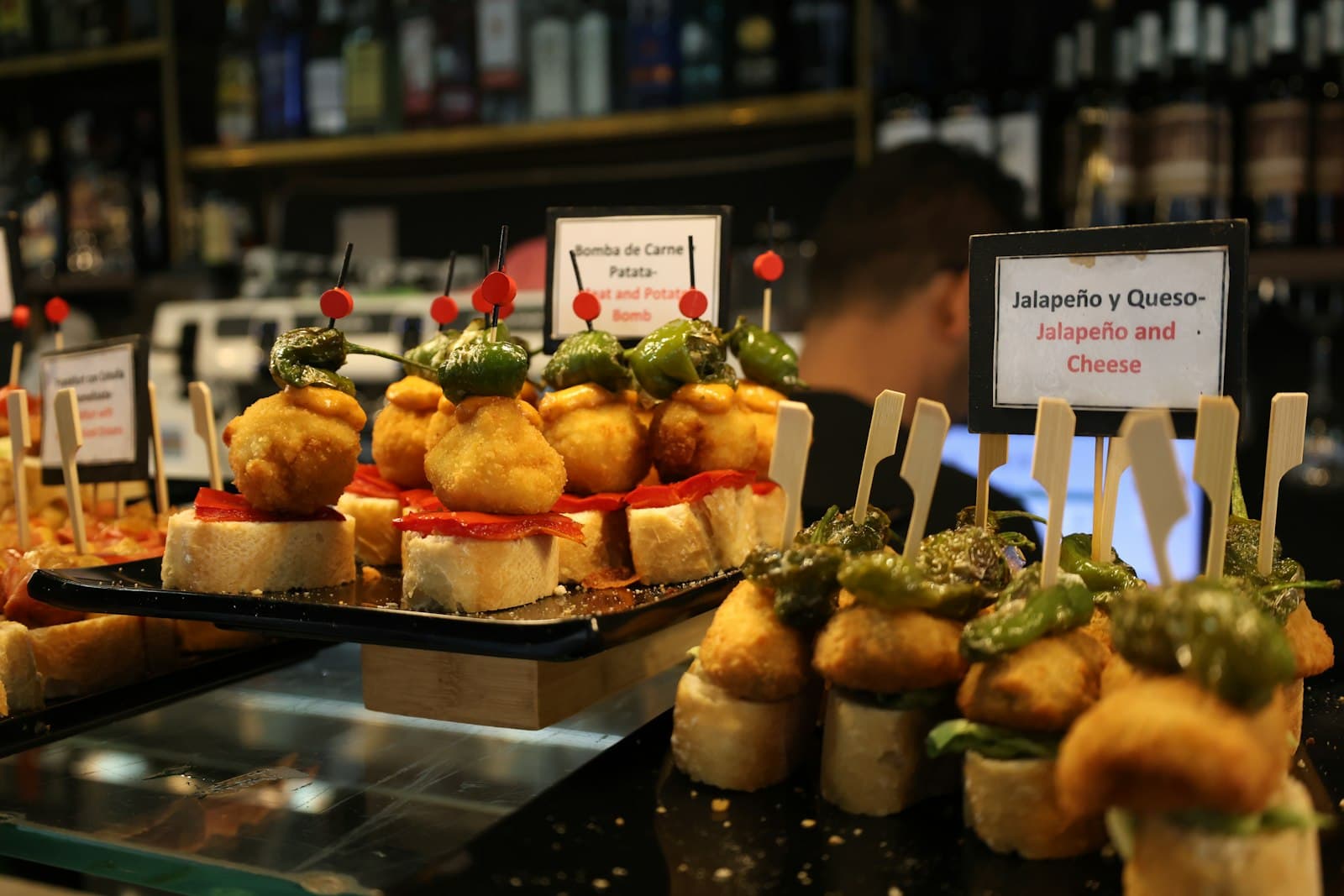 Pintxos con pimiento y queso sobre la barra de un bar, con carteles escritos a mano