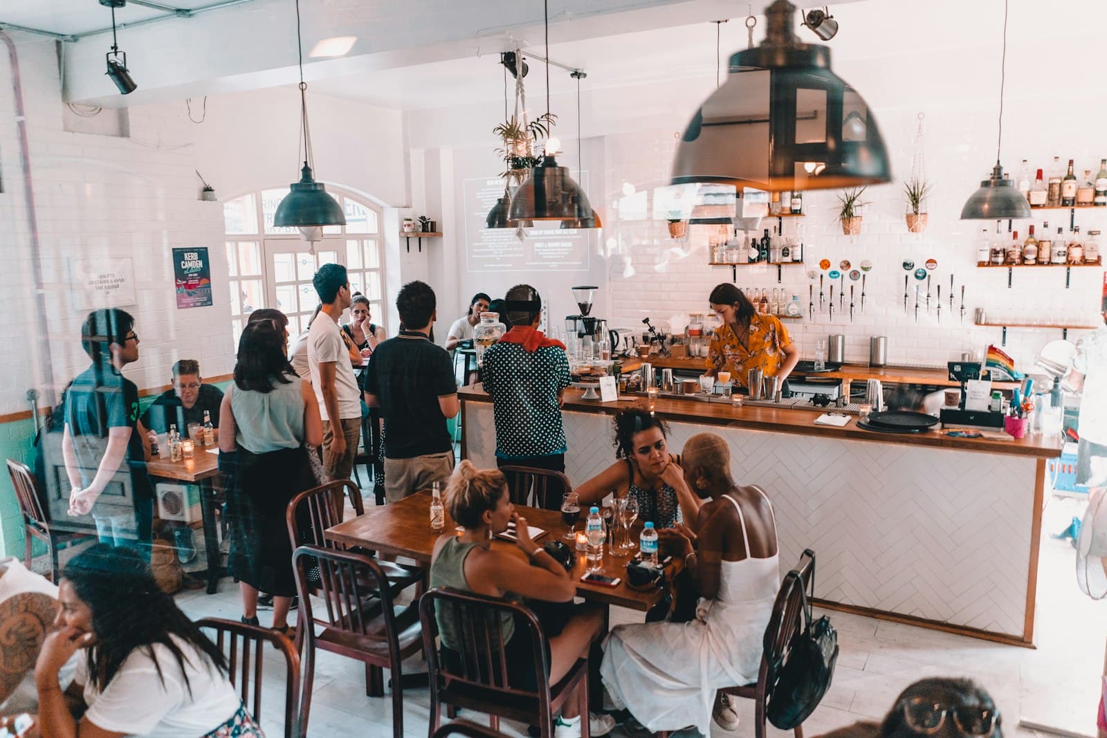 Cafetería luminosa con clientes pidiendo en la barra y mesas llenas a media mañana