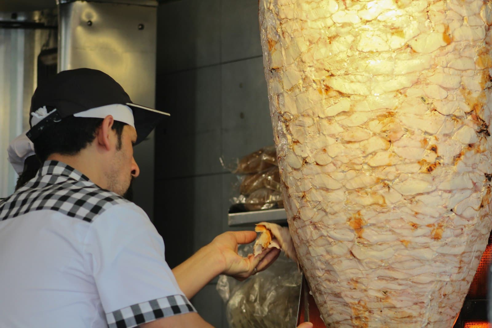 Cocinero con gorra cortando carne de un döner de pollo en el asador vertical